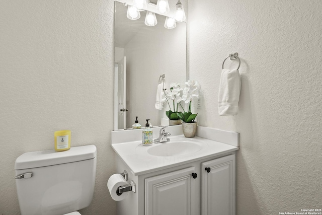 half bathroom featuring toilet, a textured wall, and vanity