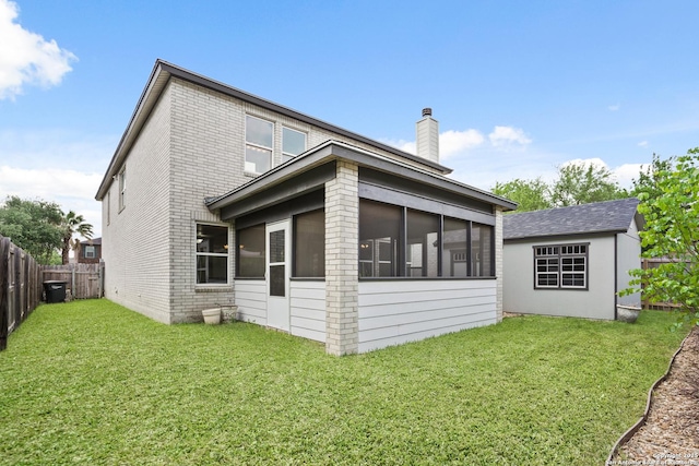 rear view of house featuring a chimney, brick siding, fence private yard, a lawn, and a sunroom