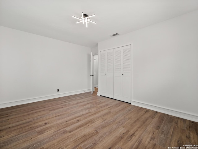 unfurnished bedroom featuring wood finished floors, a closet, baseboards, and visible vents