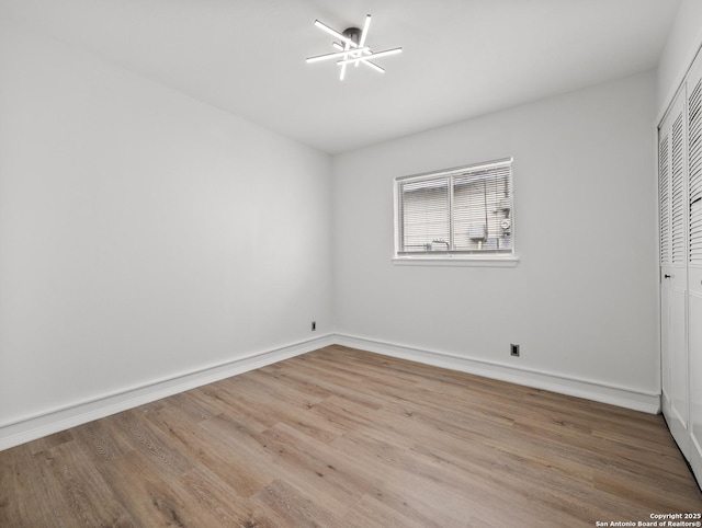 unfurnished bedroom featuring baseboards, wood finished floors, a chandelier, and a closet