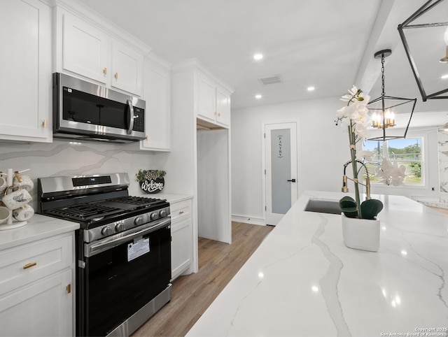 kitchen with white cabinets, a sink, a notable chandelier, and appliances with stainless steel finishes