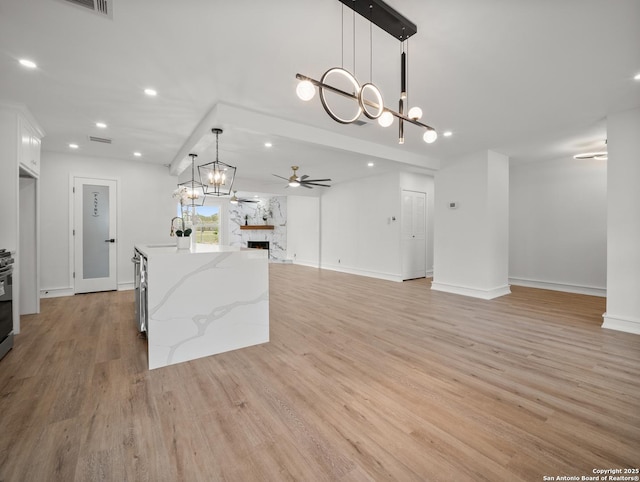 kitchen featuring white cabinets, light wood finished floors, open floor plan, recessed lighting, and ceiling fan with notable chandelier