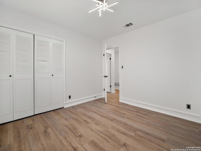 unfurnished bedroom featuring wood finished floors, a closet, baseboards, a notable chandelier, and visible vents