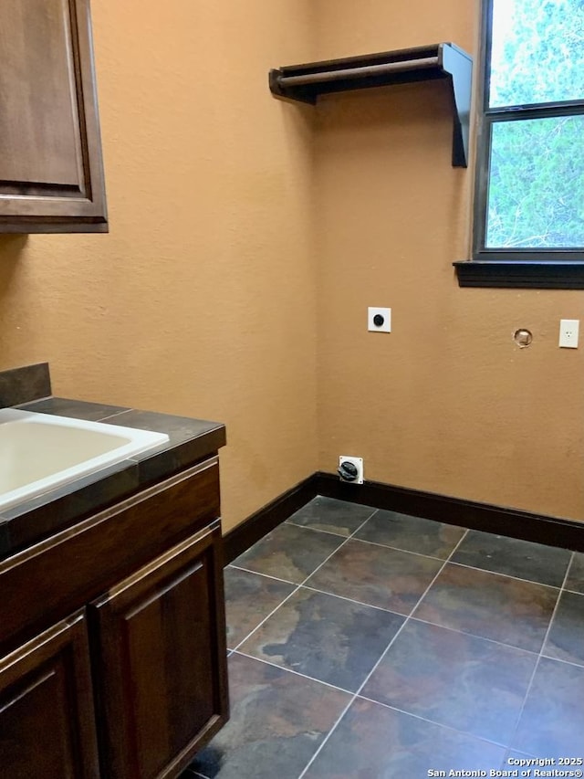 laundry room featuring dark tile patterned flooring, baseboards, hookup for an electric dryer, and cabinet space