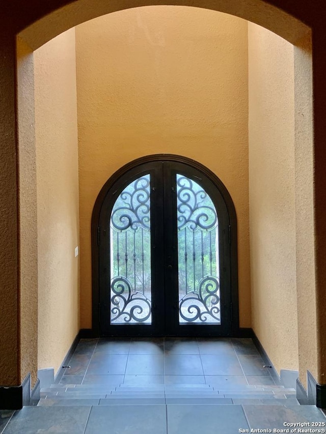 foyer featuring arched walkways, a textured wall, and french doors