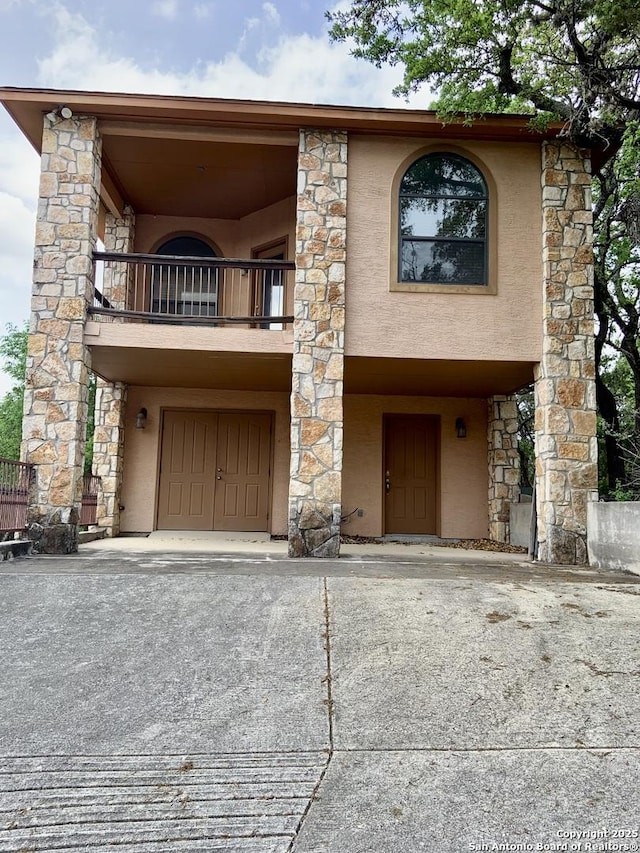 view of front of house featuring stucco siding, stone siding, and a balcony