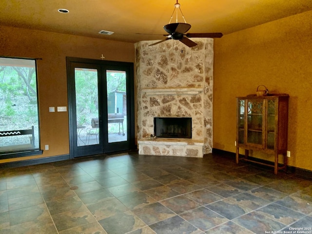 unfurnished living room featuring tile patterned floors, a stone fireplace, visible vents, baseboards, and ceiling fan