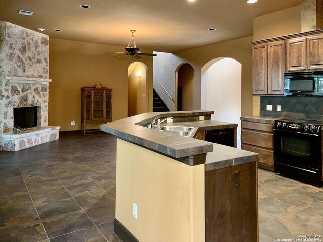 kitchen featuring a center island, a sink, black appliances, ceiling fan, and arched walkways
