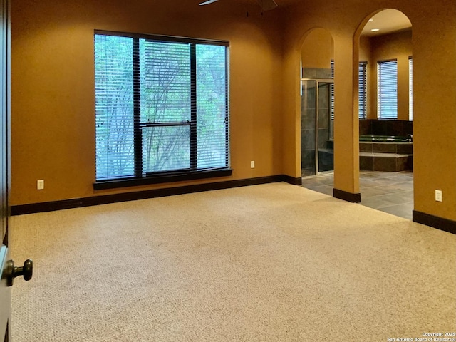 spare room featuring ceiling fan, arched walkways, carpet flooring, and baseboards