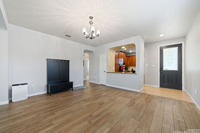 unfurnished living room with arched walkways, a chandelier, visible vents, and light wood finished floors