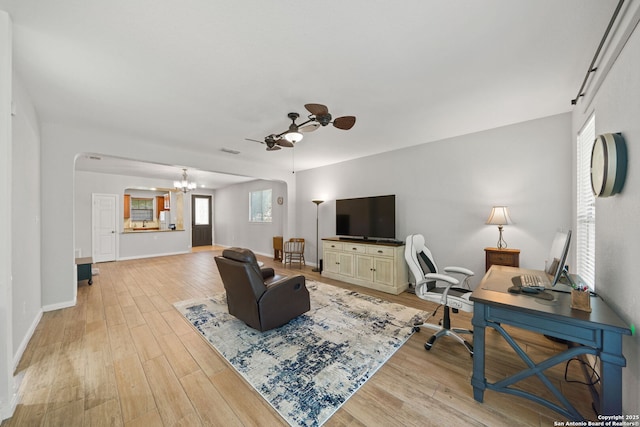 living area featuring light wood-style flooring, visible vents, baseboards, and ceiling fan with notable chandelier