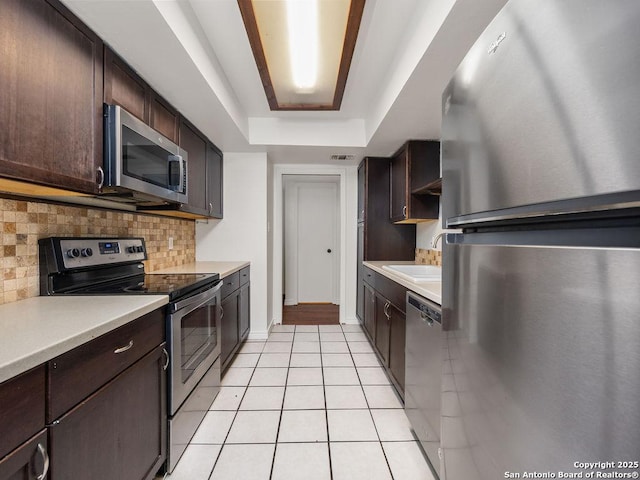 kitchen featuring dark brown cabinets, a sink, decorative backsplash, light tile patterned flooring, and stainless steel appliances