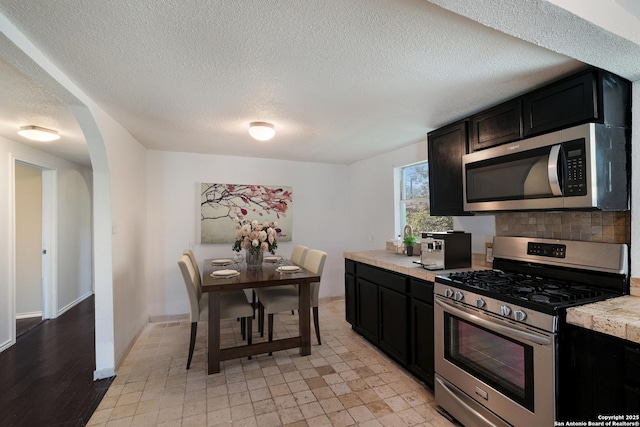 kitchen with light countertops, arched walkways, dark cabinetry, a textured ceiling, and stainless steel appliances