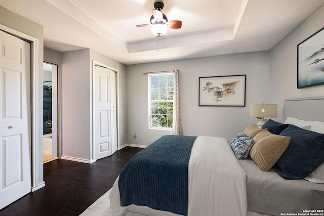 bedroom featuring a ceiling fan, wood finished floors, baseboards, a closet, and a tray ceiling