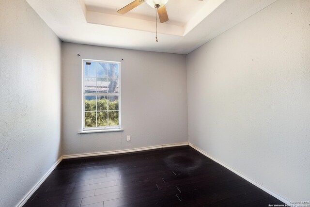 unfurnished room featuring a ceiling fan, a tray ceiling, dark wood finished floors, and baseboards