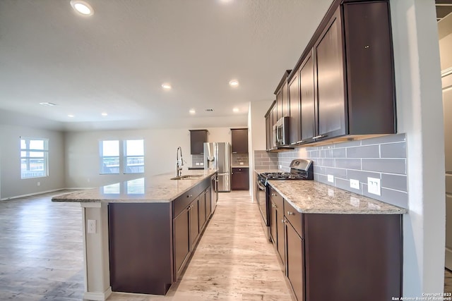kitchen with dark brown cabinets, a sink, light wood-type flooring, a center island with sink, and appliances with stainless steel finishes