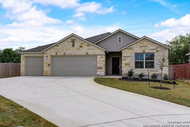 ranch-style house featuring a garage, driveway, stone siding, and fence