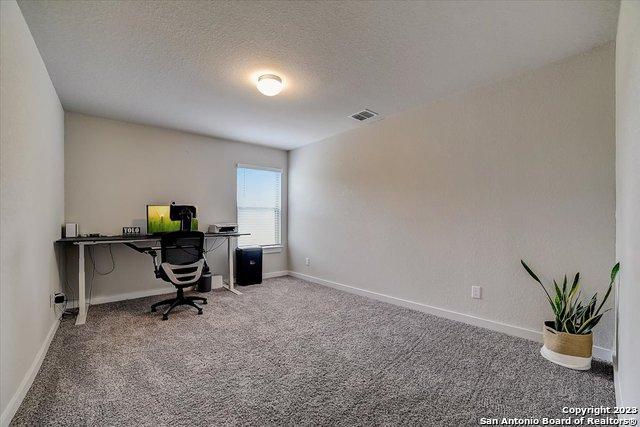 carpeted home office with baseboards, a textured ceiling, and visible vents