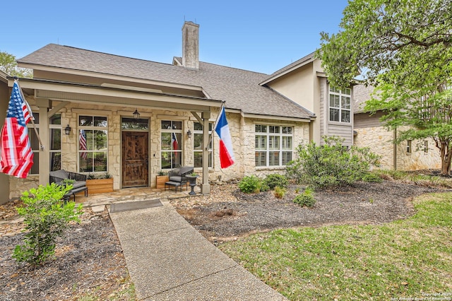 view of front of property with roof with shingles, covered porch, a chimney, and stone siding