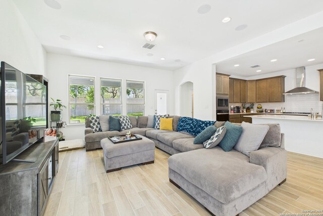 living area with light wood-type flooring, arched walkways, visible vents, and recessed lighting