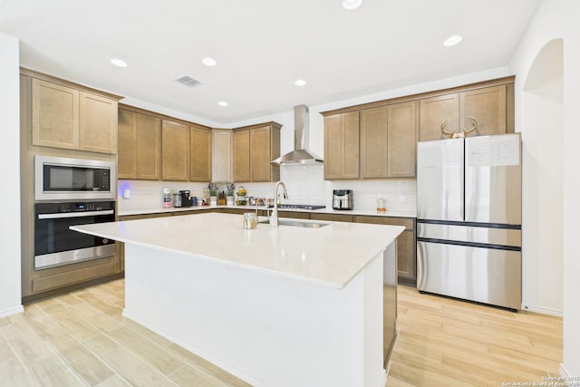 kitchen with light wood finished floors, stainless steel appliances, visible vents, and wall chimney range hood
