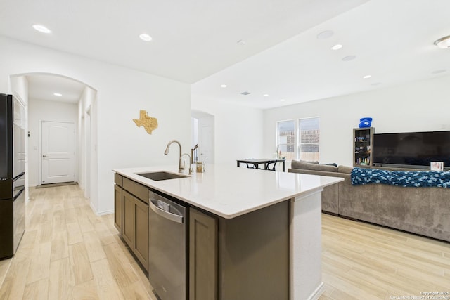 kitchen featuring arched walkways, stainless steel dishwasher, a sink, and light wood-type flooring