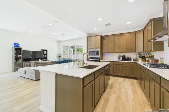 kitchen featuring wall chimney exhaust hood, light wood finished floors, a sink, and visible vents