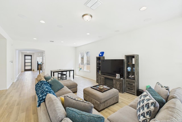 living area featuring light wood-style flooring, visible vents, arched walkways, and recessed lighting
