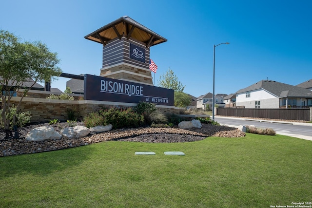 community / neighborhood sign featuring a yard and fence