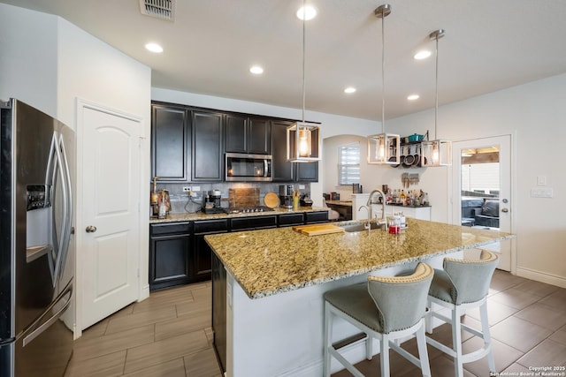 kitchen featuring a sink, visible vents, light stone counters, an island with sink, and appliances with stainless steel finishes