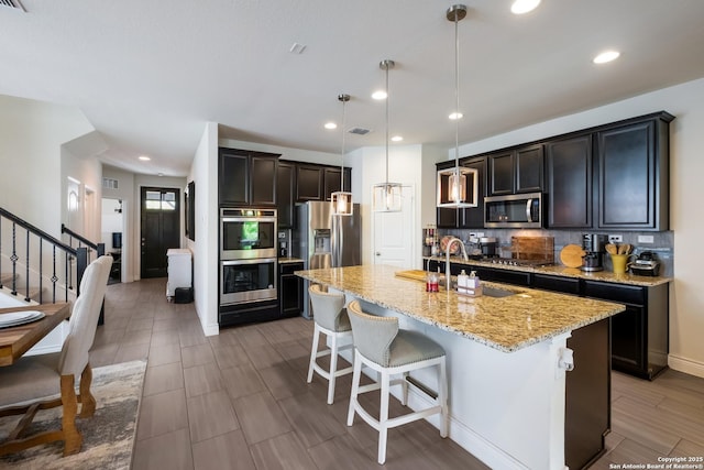 kitchen featuring a kitchen breakfast bar, light stone counters, a sink, decorative backsplash, and appliances with stainless steel finishes