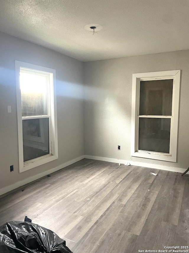 spare room featuring wood finished floors, a textured ceiling, and baseboards