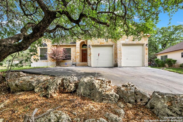 view of property hidden behind natural elements with stone siding and aphalt driveway