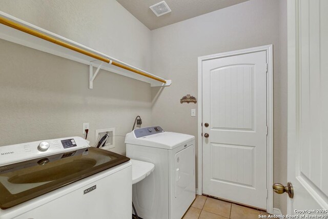 laundry room with washing machine and dryer, visible vents, light tile patterned flooring, and laundry area