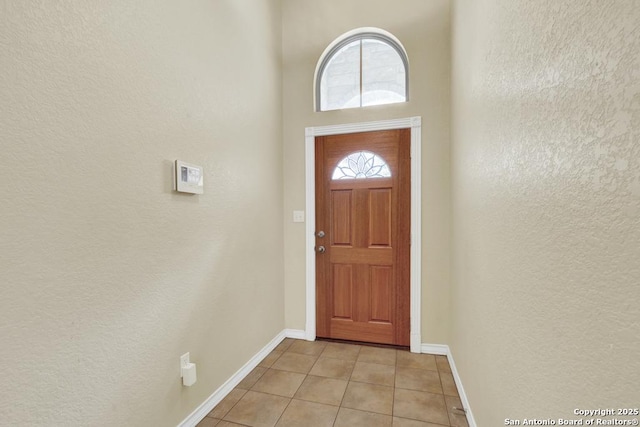 doorway featuring a textured wall, baseboards, a towering ceiling, and light tile patterned floors
