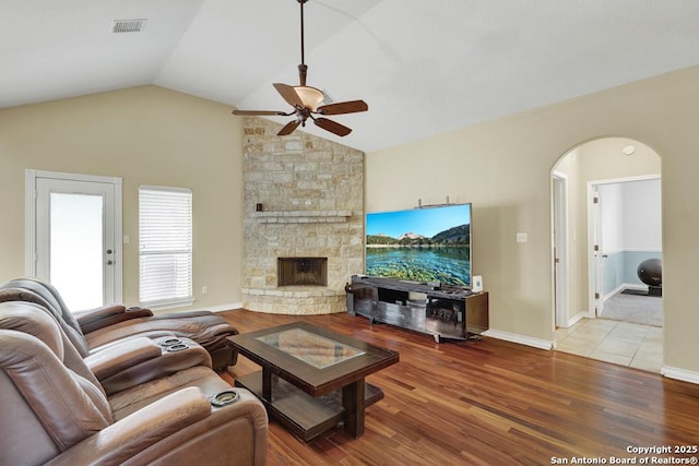 living room featuring vaulted ceiling, wood finished floors, ceiling fan, arched walkways, and a fireplace