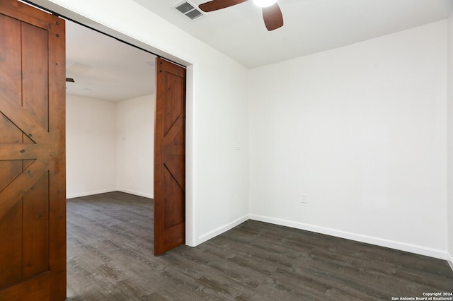 spare room featuring dark wood-style flooring, a barn door, visible vents, baseboards, and a ceiling fan
