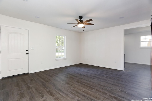 empty room featuring a wealth of natural light, a ceiling fan, dark wood-style floors, and baseboards