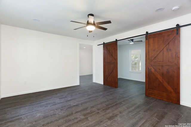 unfurnished bedroom featuring baseboards, dark wood-type flooring, ceiling fan, and a barn door