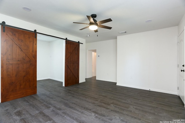 unfurnished bedroom featuring a barn door, baseboards, and dark wood-style floors