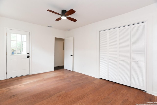 unfurnished bedroom featuring wood finished floors, visible vents, a closet, baseboards, and ceiling fan