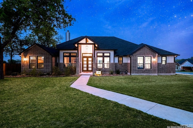 view of front facade with french doors, a chimney, fence, brick siding, and a front yard