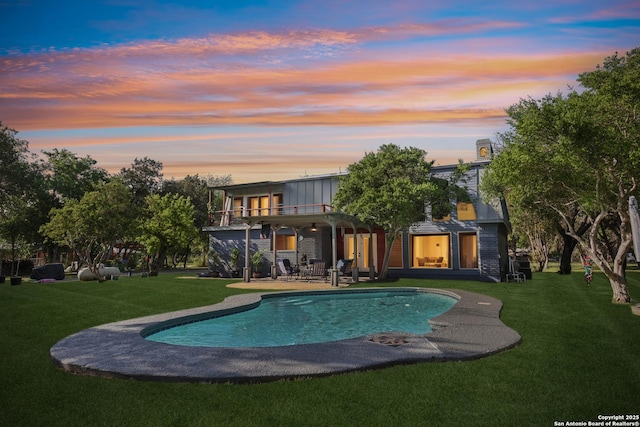 back of house at dusk featuring a patio area, a lawn, an outdoor pool, and a balcony