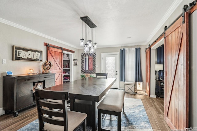 dining room with a barn door, crown molding, and wood finished floors