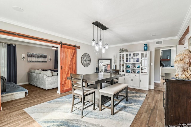 dining area featuring a barn door, wood finished floors, baseboards, ornamental molding, and visible vents