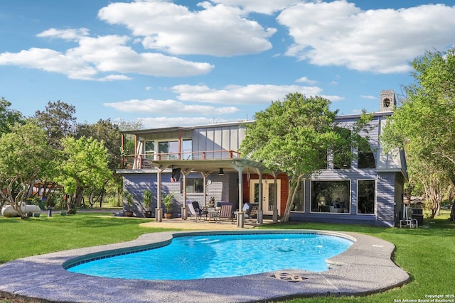 back of property with a balcony, an outdoor pool, board and batten siding, a yard, and a patio