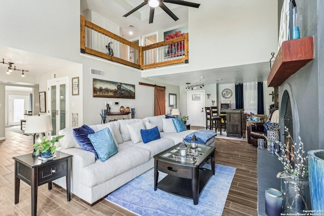 living room with a barn door, a ceiling fan, wood tiled floor, a towering ceiling, and visible vents