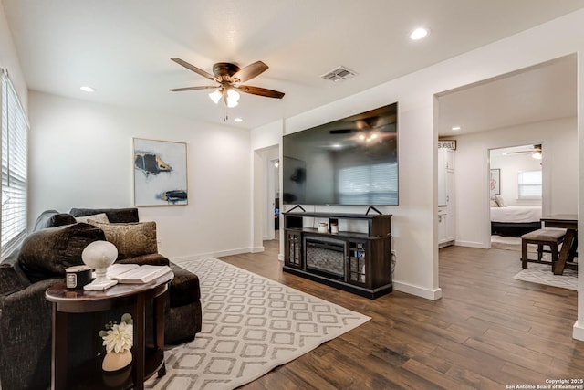 living area with baseboards, wood finished floors, visible vents, and ceiling fan