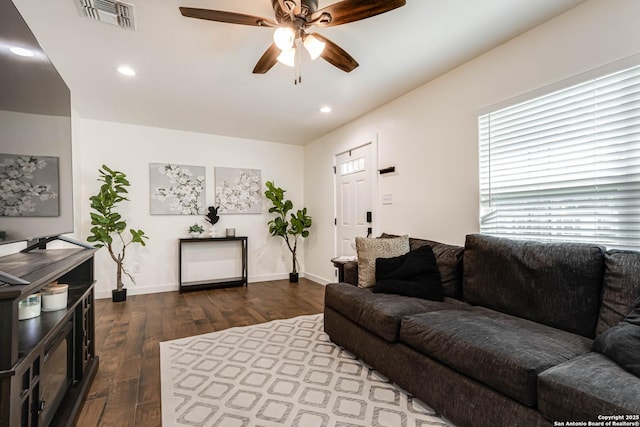 living room featuring dark wood-type flooring, visible vents, baseboards, and ceiling fan