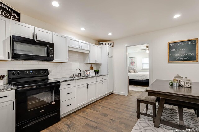 kitchen with white cabinets, a sink, dark wood finished floors, decorative backsplash, and black appliances